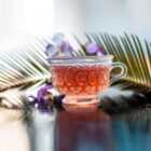 Tasse de rooibos orangé avec feuille de palmier et fleurs violettes ambiance tropicale