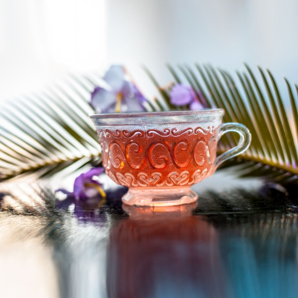 Tasse de rooibos orangé avec feuille de palmier et fleurs violettes ambiance tropicale