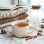 Tasse de rooibos orangé avec pulls tricotés livre ouvert pommes de pin et cannelle ambiance cocooning hivernal
