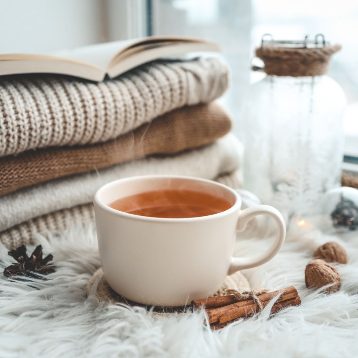 Tasse de rooibos orangé avec pulls tricotés livre ouvert pommes de pin et cannelle ambiance cocooning hivernal