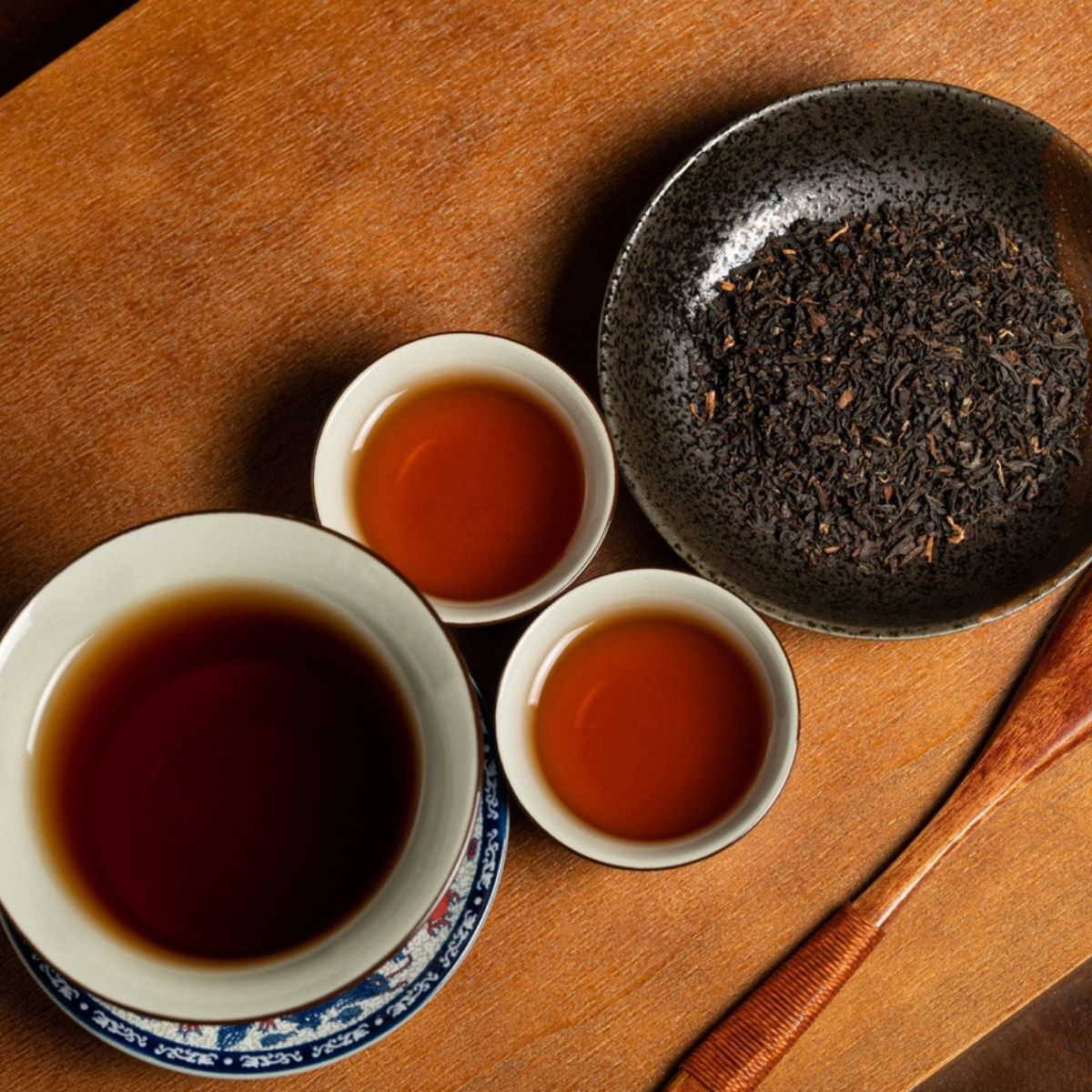 Feuilles de Pu-erh vrac dans un bol et infusion bourgogne aux reflets orangés dans des tasses chinoises