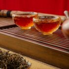 Deux tasses en verre avec infusion de Pu-erh orangée sur plateau gongfu avec théière Yixing