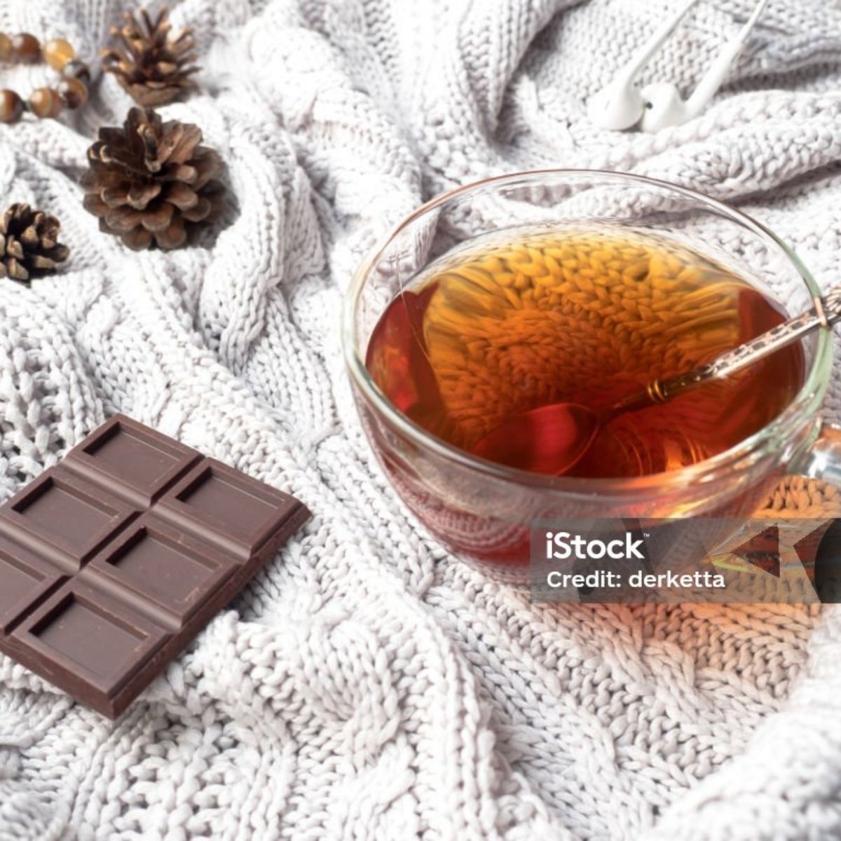 Tasse de rooibos ambré avec tablette de chocolat noir sur fond de tricot blanc et pommes de pin