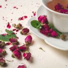 Tasse de rooibos orangé avec boutons de rose séchés et feuilles de menthe sur fond blanc