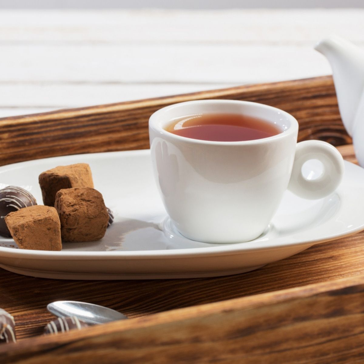 Tasse de rooibos rouge-ambré avec truffes au chocolat sur plateau en bois et théière blanche
