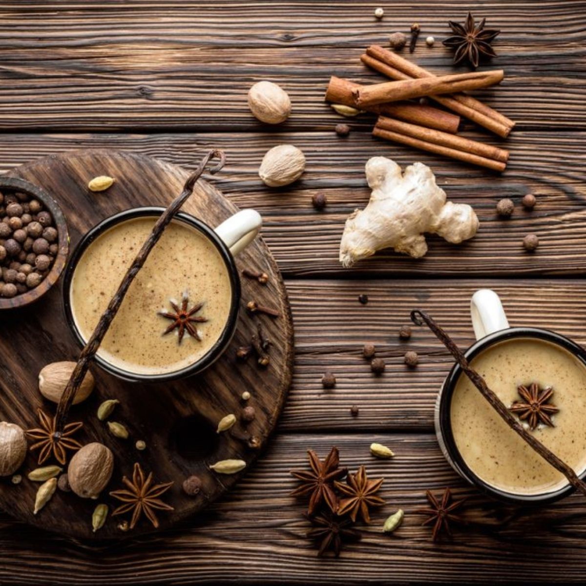 Deux tasses de chai latte avec épices — gingembre, cannelle, anis étoilé, cardamome et vanille sur fond de bois