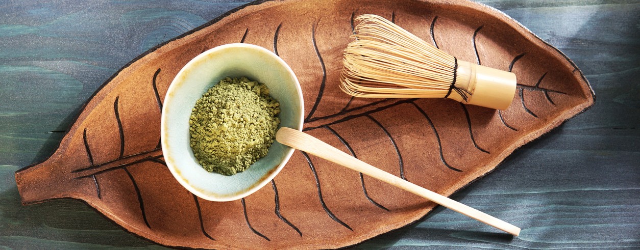 Poudre de matcha dans un bol avec chasen et cuillère sur plateau en forme de feuille