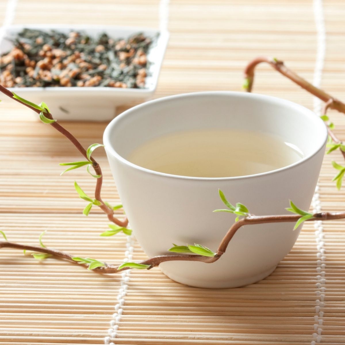 Tasse de thé vert genmaicha vert-doré avec mélange feuilles et riz soufflé en arrière-plan sur napperon bambou