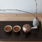 Deux tasses de thé vert sencha en céramique artisanale avec théière brune sur plateau noir ambiance zen japonaise